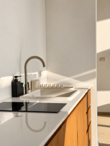 White kitchen countertop with a cooktop, sink and wooden cabinetry.