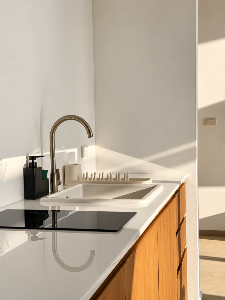 White kitchen countertop with a cooktop, sink and wooden cabinetry.