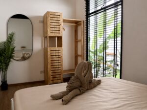 Bed with towel decorations beside a wooden wardrobe and oval wall mirror.