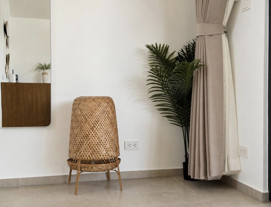 Woven chair beside an indoor palm and floor-length curtains.