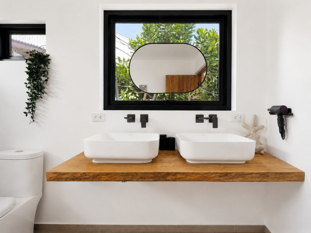 Two countertop basins on a wooden vanity beneath a round mirror and window.