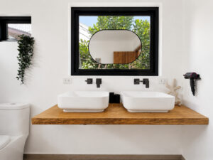 Two countertop basins on a wooden vanity beneath a round mirror and window.