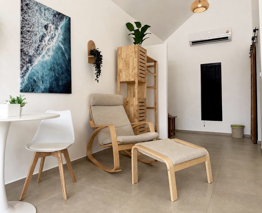 Armchair and footstool beside the dining table, wardrobe and coastal wall art.