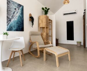 Armchair and footstool beside the dining table, wardrobe and coastal wall art.