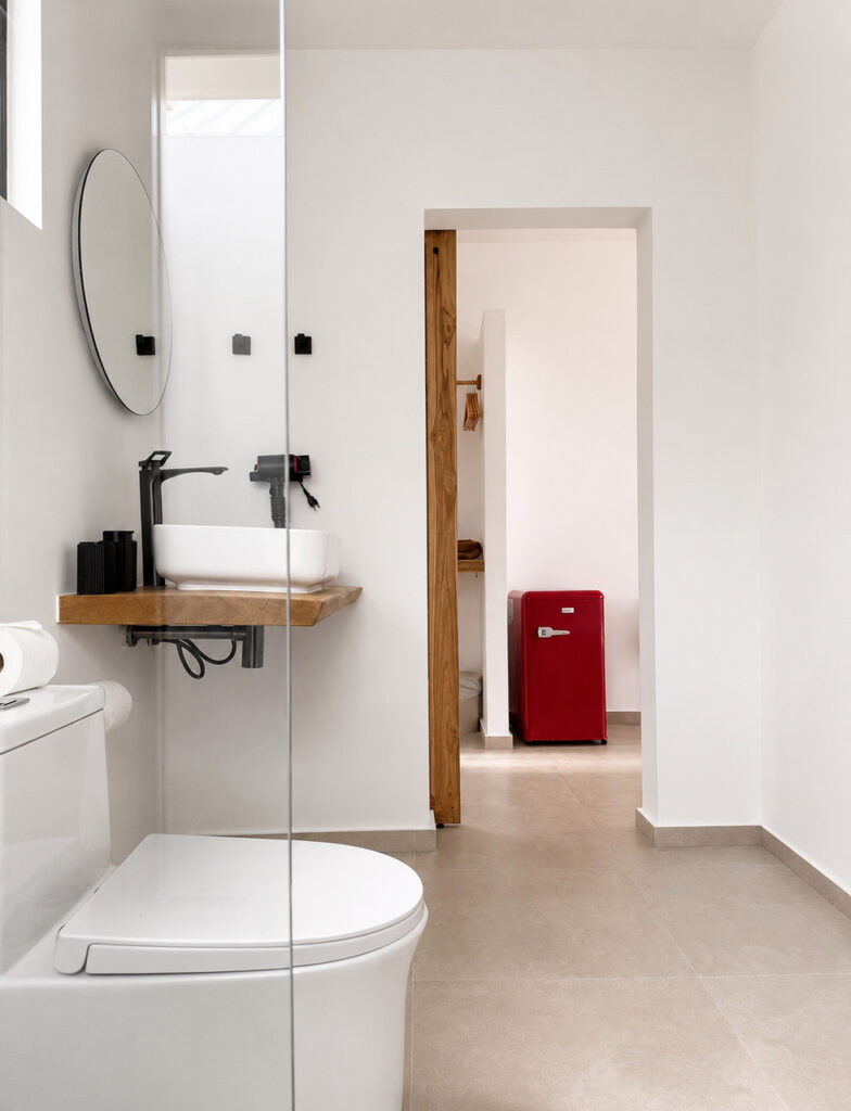 Bathroom vanity, wall mirror and toilet with the bedroom visible through the doorway.