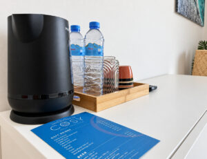 Electric kettle, cups, glasses and drinking water on a tray on the white sideboard.