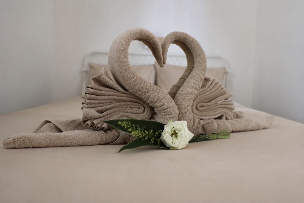 Two folded towel swans and flowers arranged on the bed.