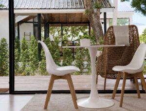 White dining table and chairs beside open glass doors with terrace greenery beyond.