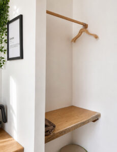 Wooden wardrobe rail, clothes hangers and shelf beside a narrow window.