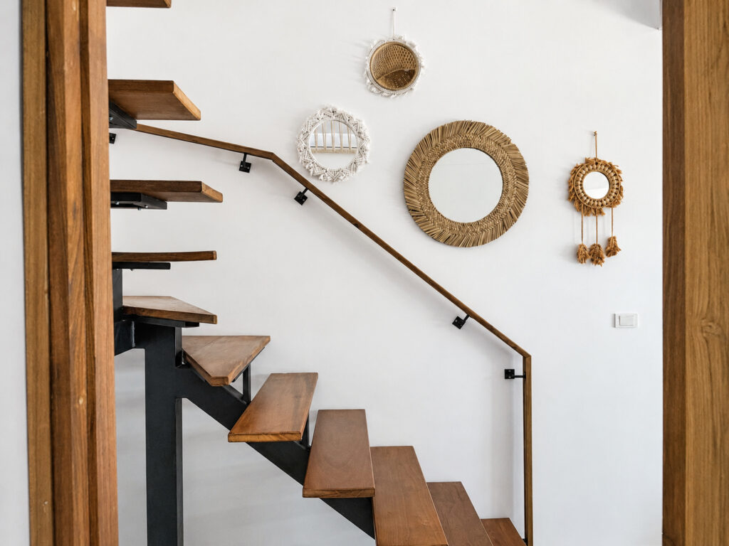 Wooden staircase and round woven mirrors on the white wall.