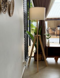 Wooden tripod floor lamp beside curtains and the tall glass doors.