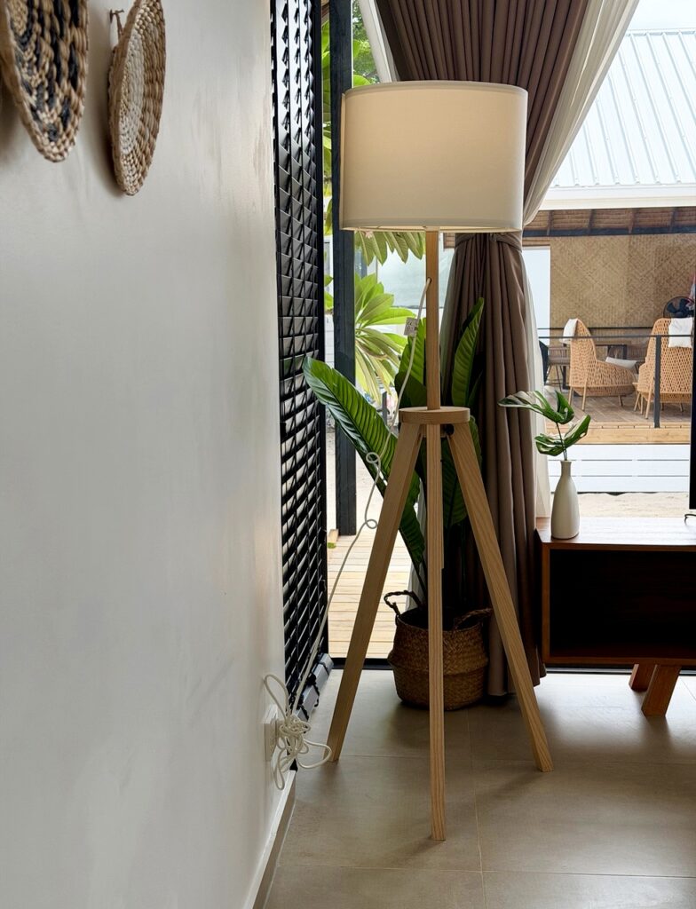 Wooden tripod floor lamp beside curtains and the tall glass doors.