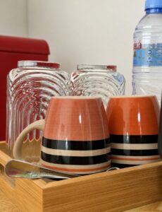 Cups, glasses and drinking water on a wooden tray beside the mini refrigerator.
