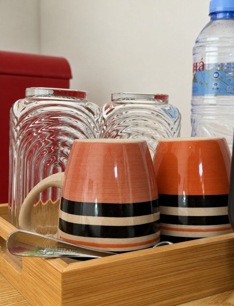 Cups, glasses and drinking water on a wooden tray beside the mini refrigerator.