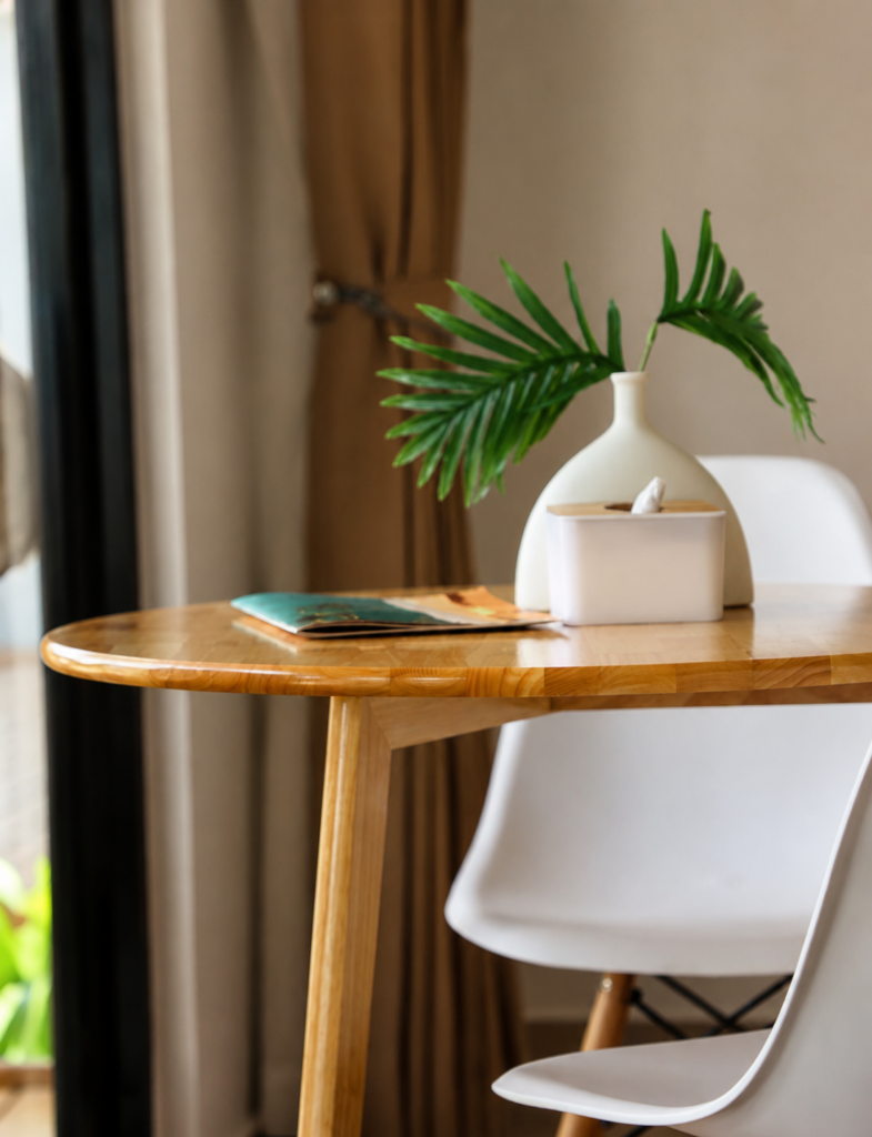 Wooden dining table with a white chair, small vase and tissue box.