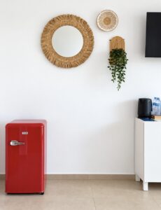 Red mini refrigerator and white sideboard beneath woven mirrors and a hanging plant.