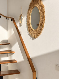 Round woven-framed mirror and wooden handrail beside the staircase.