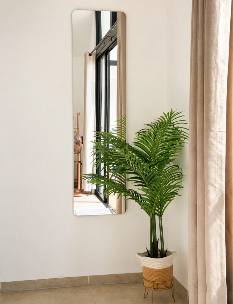 Indoor palm in a woven basket beside a wall mirror and curtains.