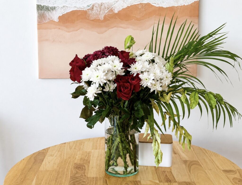 Red and white flowers in a glass vase on the wooden dining table.