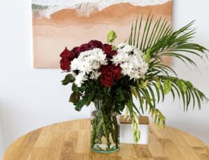 Red and white flowers in a glass vase on the wooden dining table.