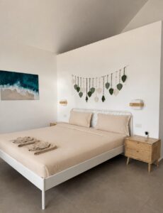 Double bed with folded towels, wooden bedside tables and leaf wall decor.