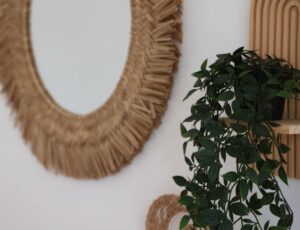 Woven-framed mirror and hanging greenery beside the wardrobe.