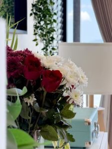 Red and white flowers beside a floor lamp and a mint-coloured case on a sideboard.