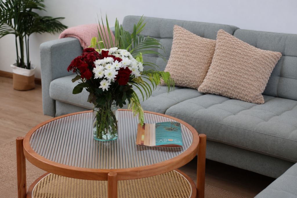 Grey sofa and round glass-topped coffee table with a vase of flowers.
