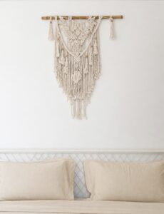 Macrame wall hanging above the cream bed pillows.