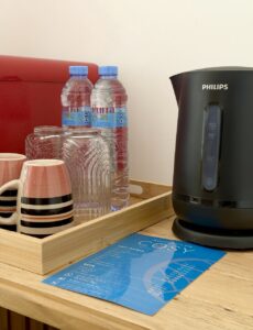 Electric kettle, cups, glasses and drinking water on a wooden refreshment stand.