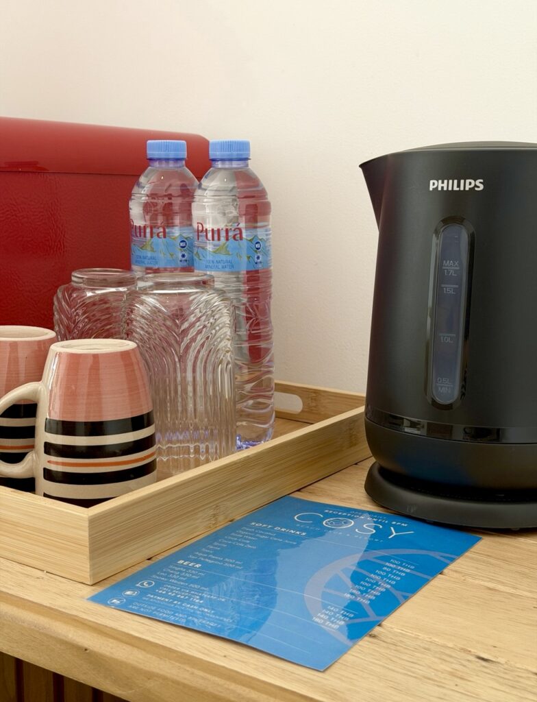 Electric kettle, cups, glasses and drinking water on a wooden refreshment stand.