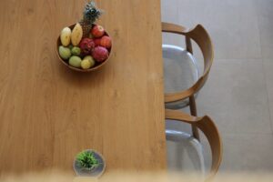 Overhead view of a bowl of fruit on a wooden dining table.