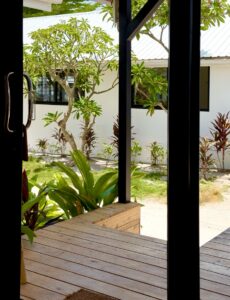 Open glass doors overlooking the wooden terrace, plants and a leafy tree.
