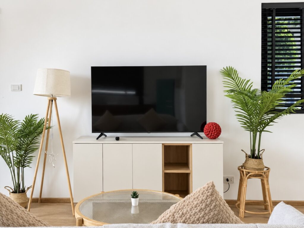 Television above a white sideboard with indoor palms and a round coffee table.