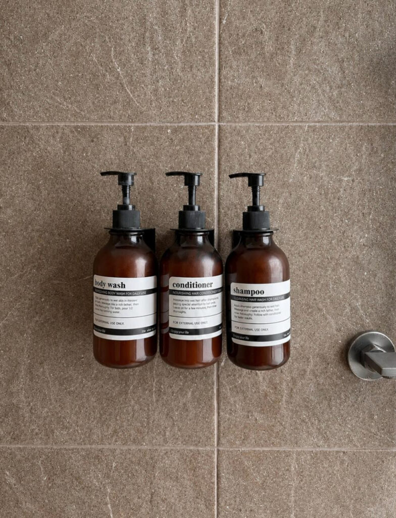 Three wall-mounted toiletry dispensers against the shower wall.