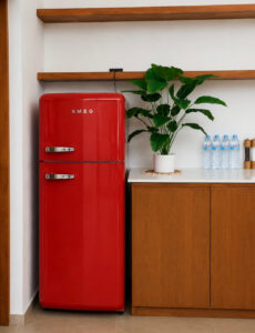 Red refrigerator beside the wooden kitchen cabinetry and open shelves.