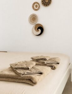 Folded towels on the bed beneath round woven wall decorations.