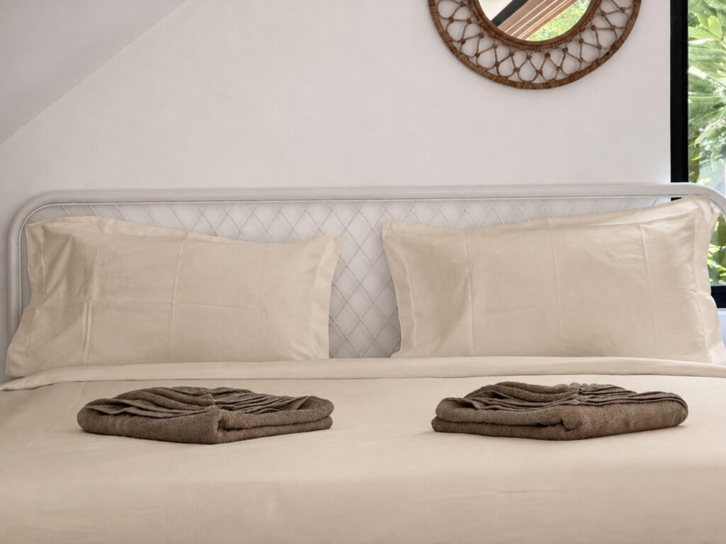 Loft bed with light-coloured pillows, folded towels and woven wall decor.