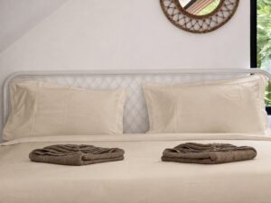 Loft bed with light-coloured pillows, folded towels and woven wall decor.