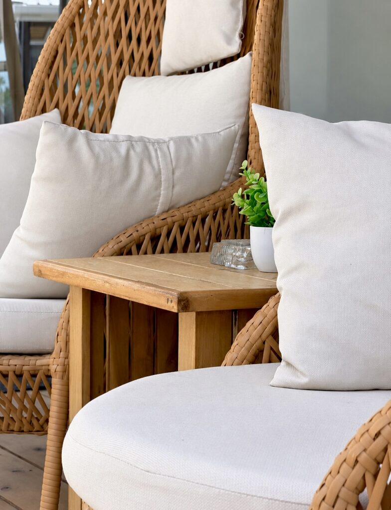 Close view of woven terrace chairs, white cushions and a wooden table.