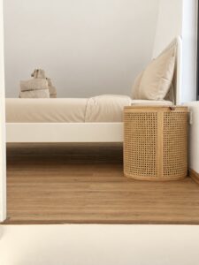 Side view of the bed and a small woven bedside table.