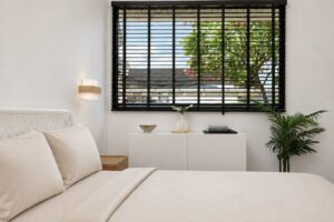 Bedside view towards a window with a black blind and a white cabinet.