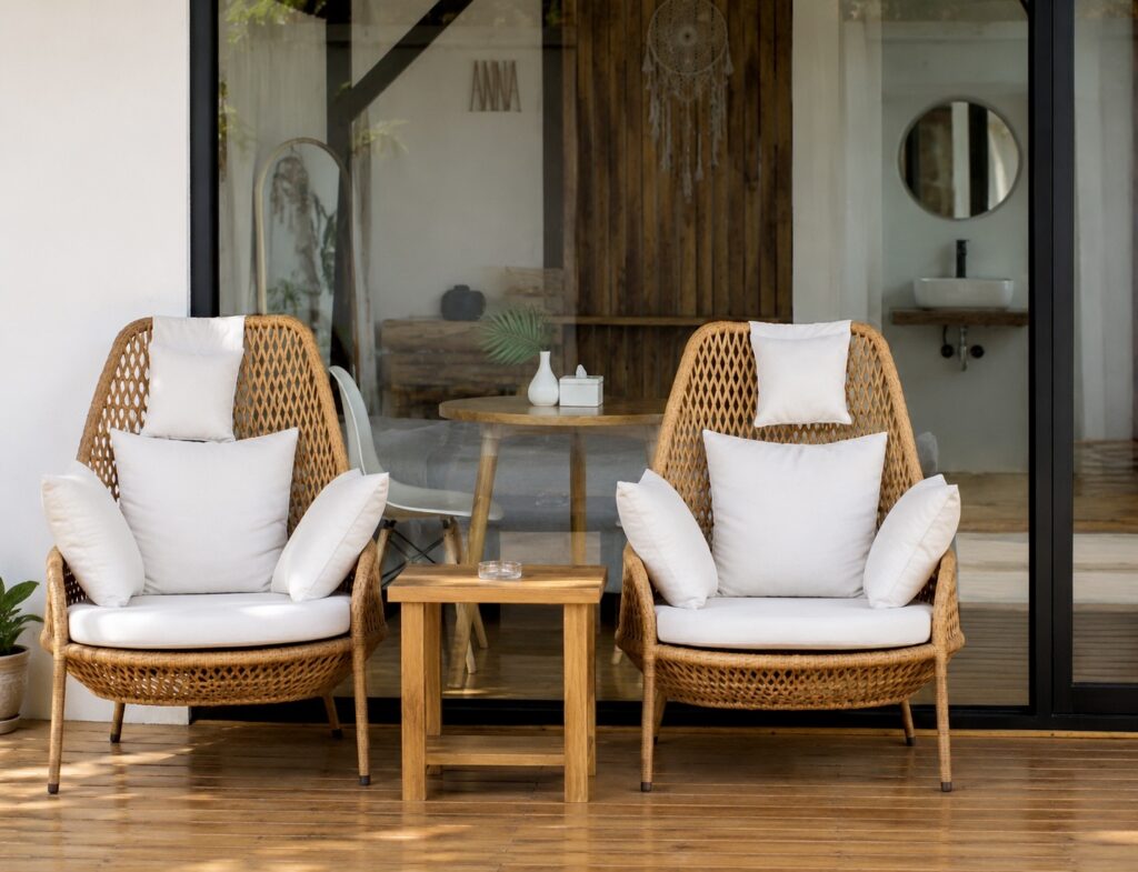 Two woven chairs and a wooden side table in front of the glass facade.