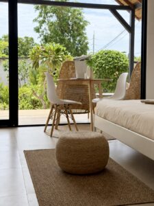 View past the bed towards the dining table and glass doors with greenery outside.