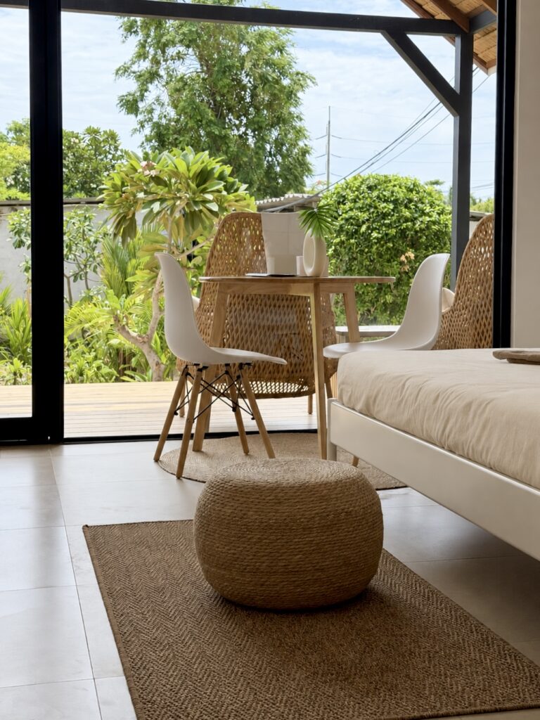 View past the bed towards the dining table and glass doors with greenery outside.